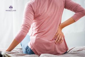 Young woman seated with her hands on her lower back from kidney endometriosis pain. - Maiden Lane Medical | New York, NY
