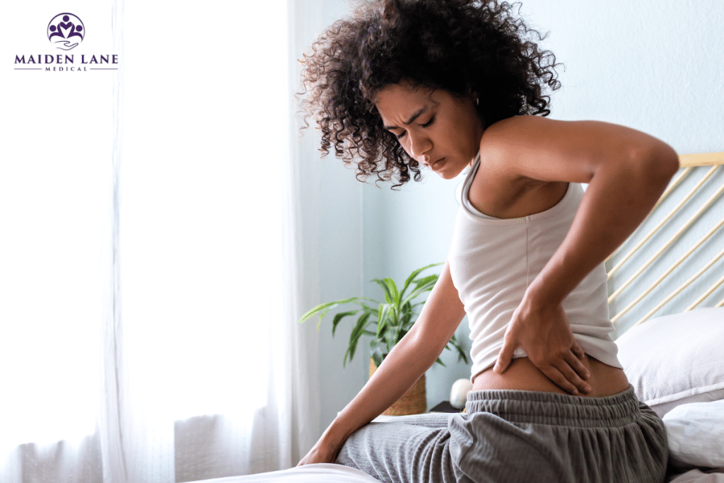A woman sitting on her bed feeling pain in her lower back caused by compression of the sciatic nerve in New York, Manhattan.